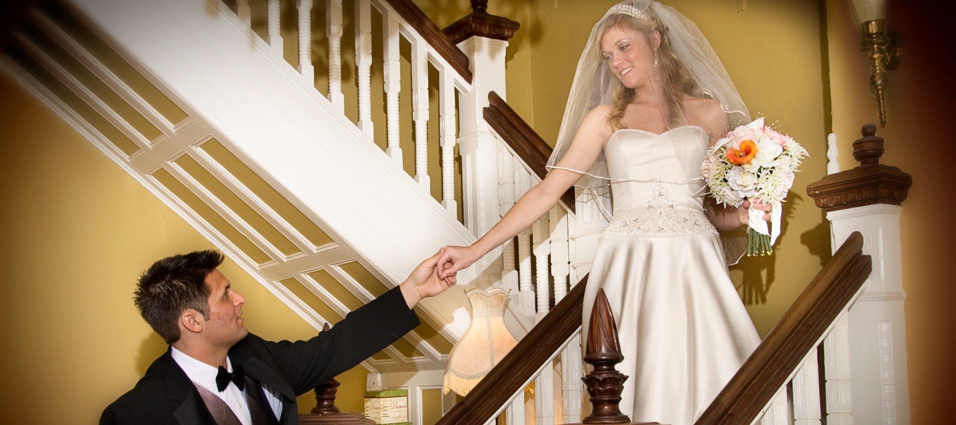 A bride standing on a staircase holding hands and looking down at her groom below