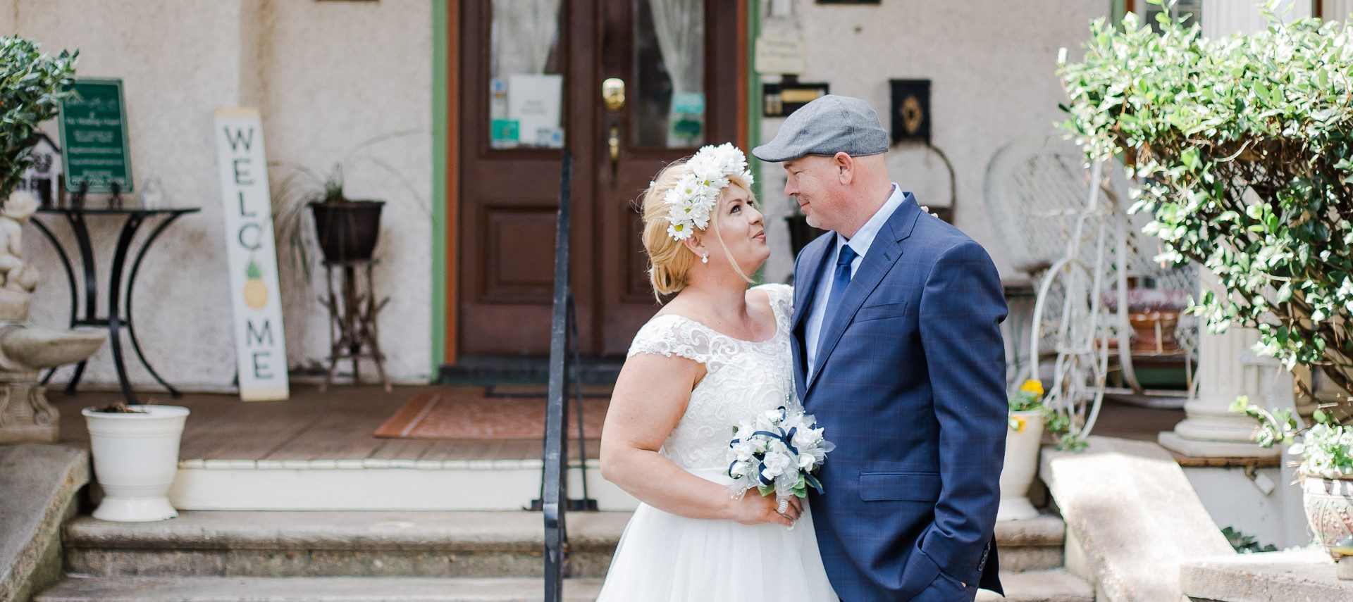 A bride and groom standing outside at the base of some steps in front of a large stately home