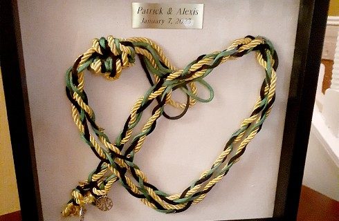 A shadow box holding a heart made out of strands of black, yellow and green rope